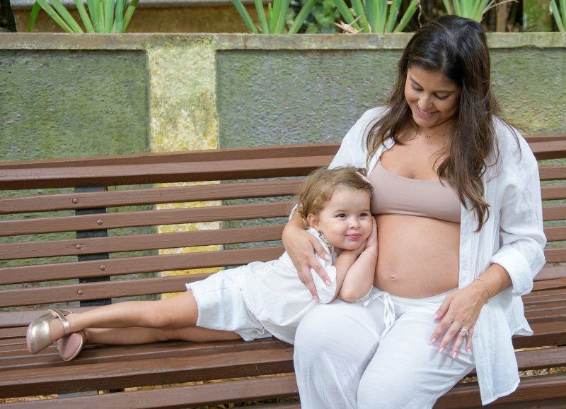 Ensaio gestante — mãe e filha no banco do parque